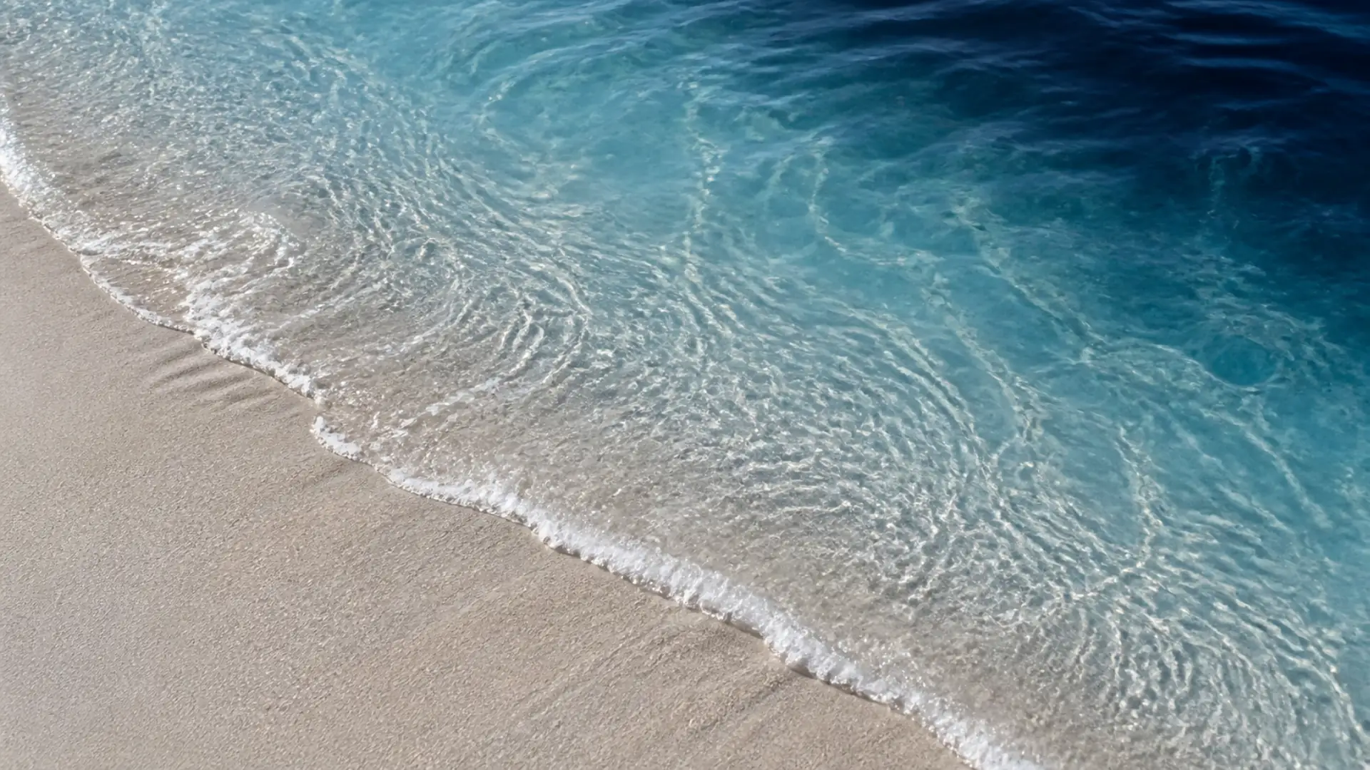 Clear blue water moving gently over pale sand