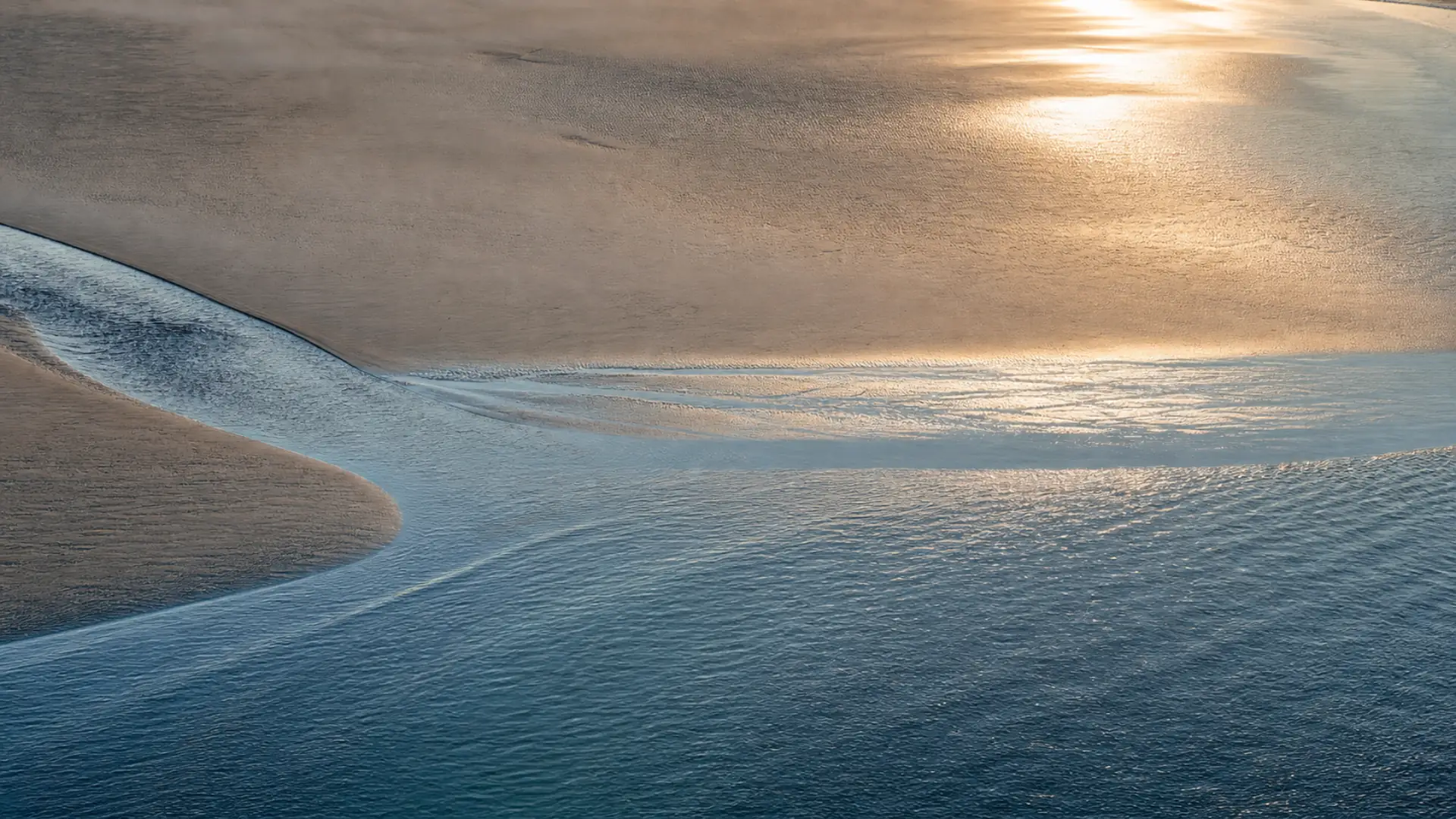 Two blue tidal channels meeting across a wide field of wet sand