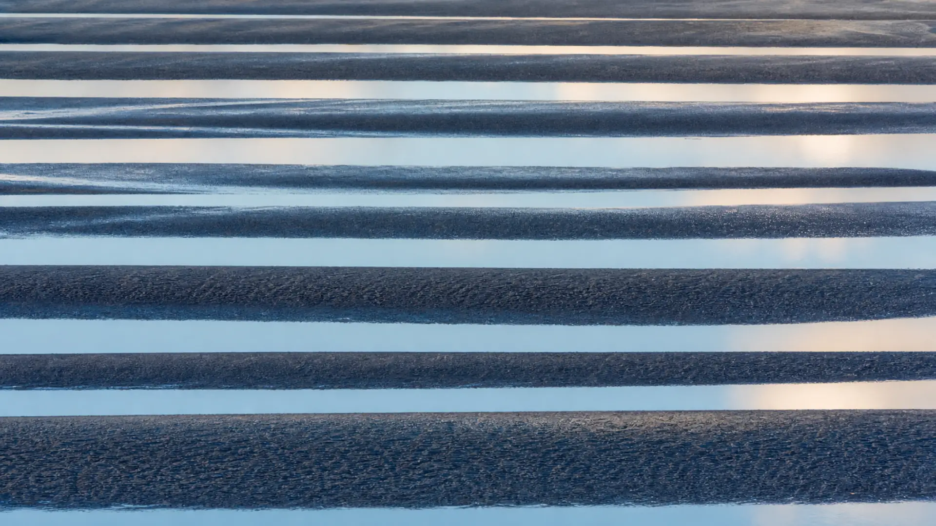 Long bands of blue reflected light crossing a quiet tide flat